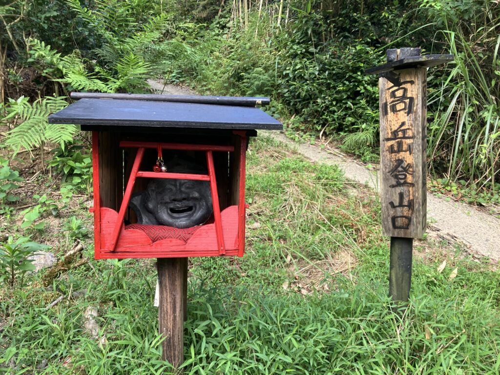 赤い祠に納められた黒い顔の像と「高岳登山口」の木製看板