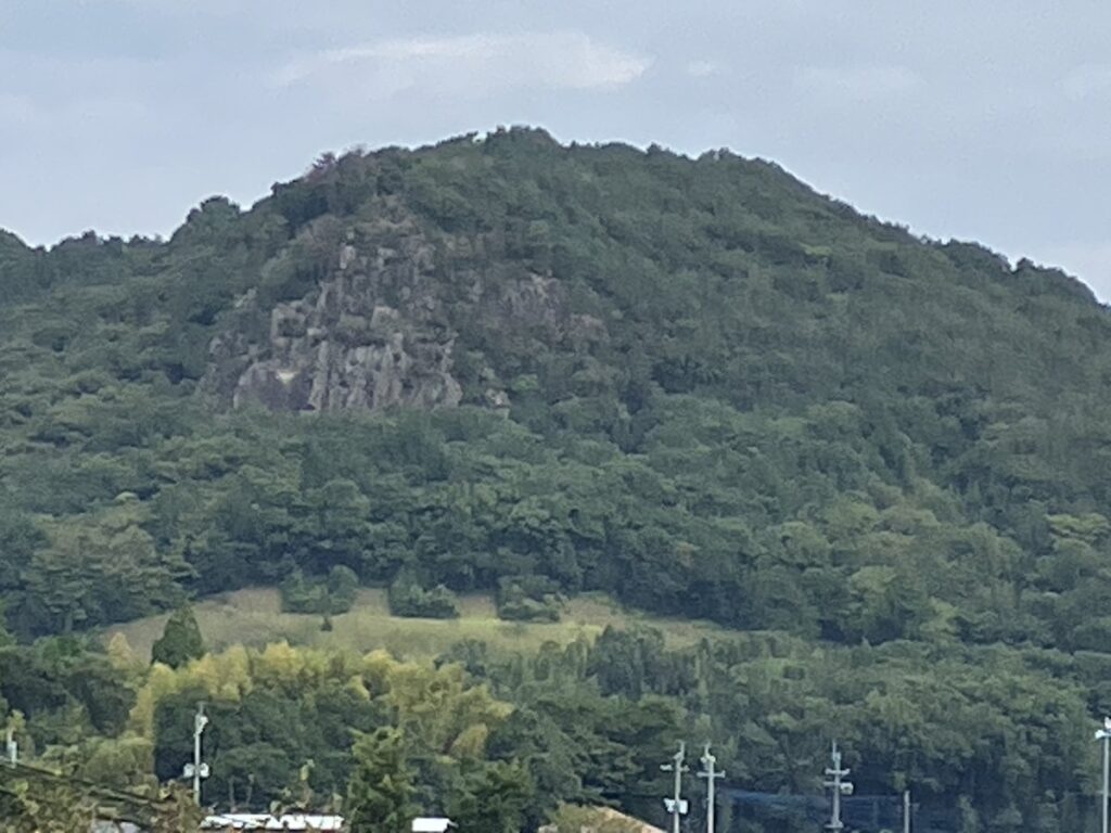 道の駅すいかの里植木のあたりから見た岩野山。手前の草地に3か所の木が並び「UCC」に見える 熊本市北区植木町