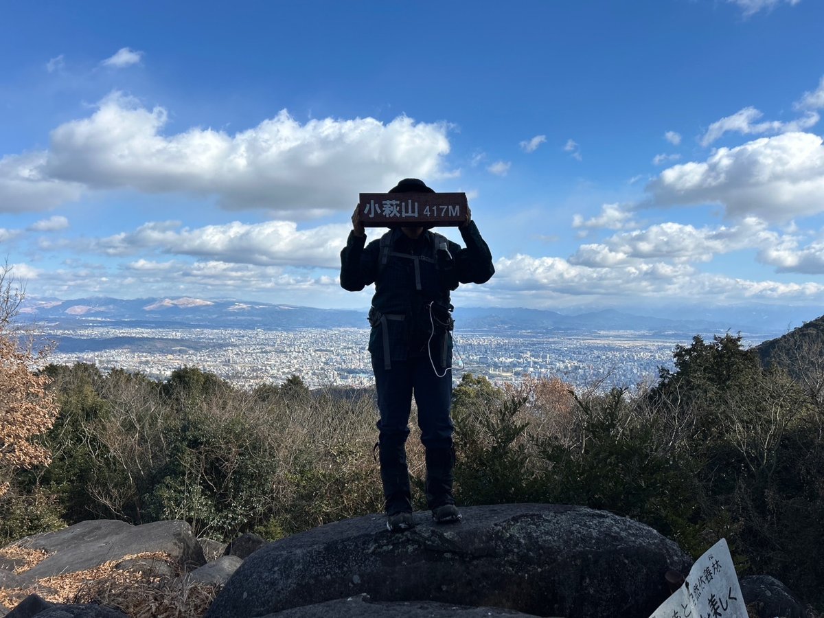 冬の山頂で山名板を掲げる後ろ姿（逆光）